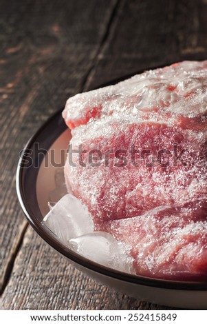 Frozen pork on the plate with ice on the wooden table vertical