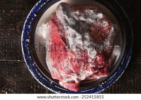Frozen pork on the blue ceramic plate on the wooden table horizontal
