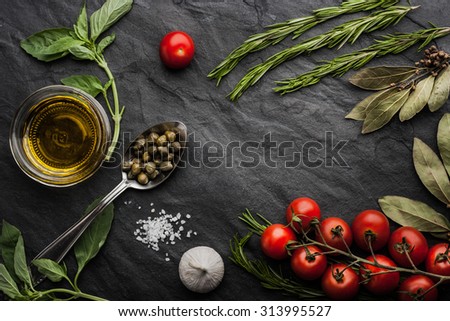 Herbs mix with tomatoes and olive oil on the black stone table