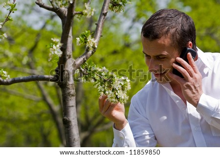 Young agronomist examining the trees in an orchard, while talking on mobile phone