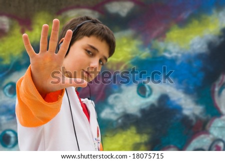 Cool teenager with his hand up, against a graffiti wall