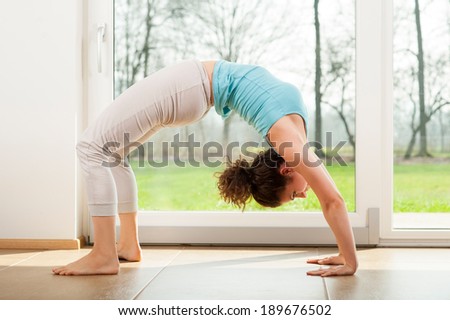 Young woman practicing yoga - Urdhva Dhanurasana / Upward bow pose indoor in front of the window - human bridge