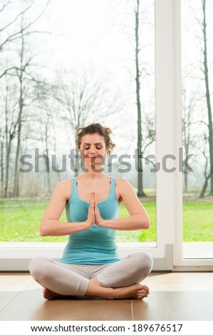 Young Caucasian woman in the prayer position. Yoga. Indoor in front of a big window.