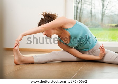 Beautiful young woman doing stretching exercise indoor in front of the window