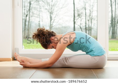 Beautiful woman doing stretching exercises indoor in front of the window