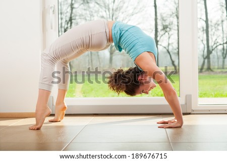 Young woman practicing yoga - Urdhva Dhanurasana / Upward bow pose indoor in front of the window
