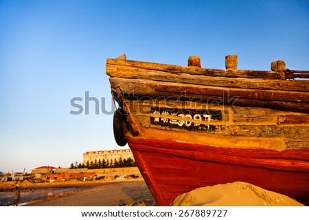 Front view of a red wooden fishing boat on beach, sea in background and blue sky.