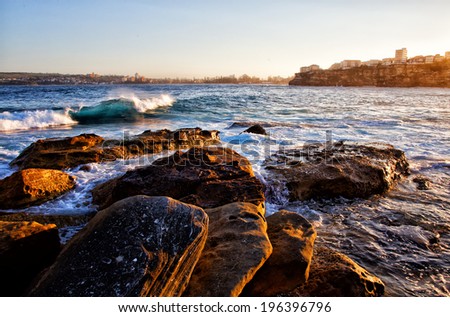 The view towards Manly from Freshwater Beach, Sydney. Colourful blue wave crashing onto rocks.