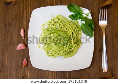 Spaghetti with pesto on wooden table with fork and garlic