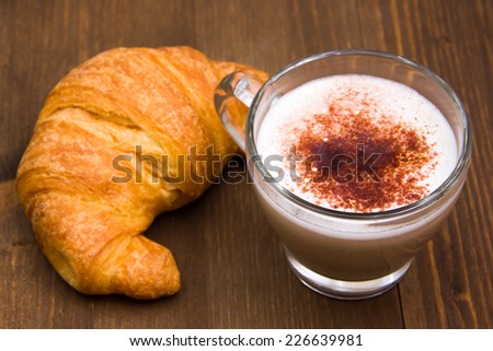 Cappuccino and croissant seen up close over wooden table