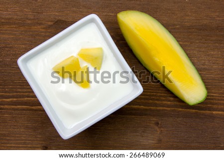 Yogurt with mango on square bowl on wooden table seen from above