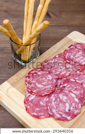 Slices of salami on cutting board and bread sticks on wooden table top