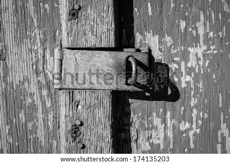 A close up of a hatch lock on an old wood door with peeling paint in black and white.
