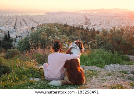 Young woman hugs her dog as they sit in a field.Athens,Greece .Real warm light from sunset.