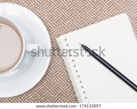 cup of coffee and notebook with pen on beige tweed fabric floor
