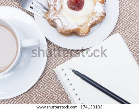 Cup of coffee with cake and note book on beige tweed fabric for breakfast or tea time