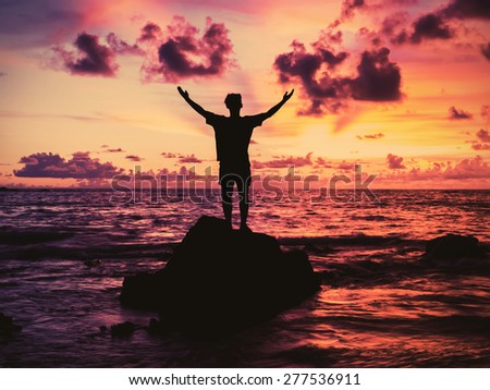 Young man open arms on the rock and look at sunset , vintage filter effect