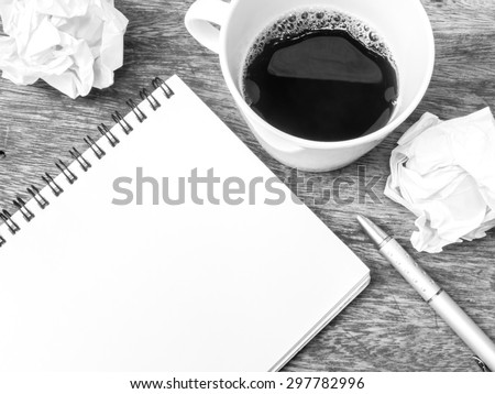 Cup of coffee , notepad and crumpled paper on wooden table, black and white color