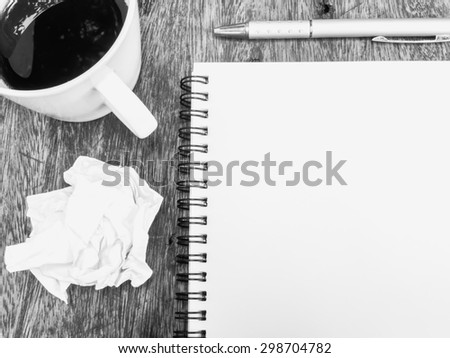 Cup of coffee , notepad and crumpled paper on wooden table, black and white color