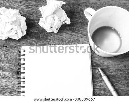empty cup of coffee , notepad and crumpled paper on wooden table, black and white color