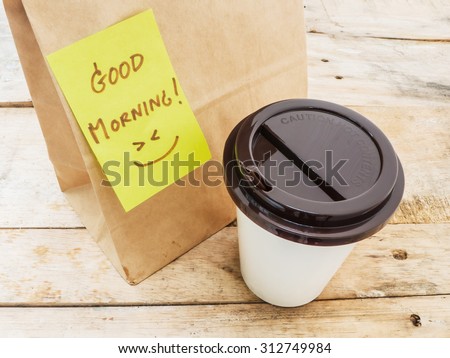 Take away cup of coffee and paper bag with note Good morning