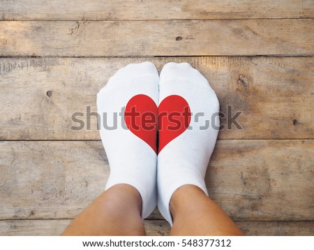 Selfie feet wearing white socks with red heart shape on wooden floor background. Love concept.