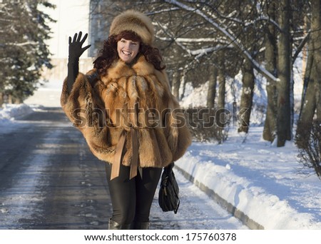The attractive woman in a fox fur coat waves a hand.