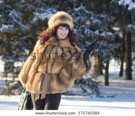 The attractive woman in a fox fur coat specifies by a hand to the right and smiles.