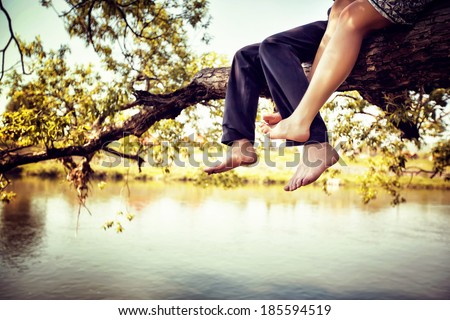Young couple in love sitting cross-legged on a tree branch above the river in nice sunny day. Photo is colorized in warm tints.