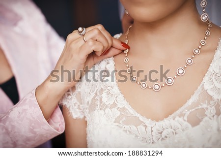 Bride preparing to wedding ceremony, her mother helps to put on jewelry