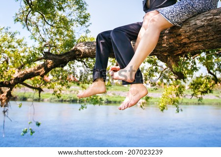 Young couple in love sitting cross-legged on a tree branch above the river in nice sunny day. Photo is effected with soft.