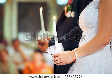 Bride and groom are holding lighted candles at the wedding ceremony in the church. Hands close-up shot