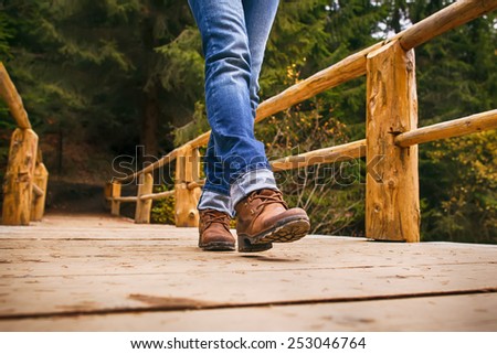 Woman in boots and blue jeans walks on wooden bridge