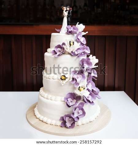 Wedding cake, decorated with purple flowers and figurines of bride and groom