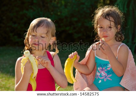 Young girls eat bananas after swiming.