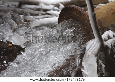 Rusty sewage pipe draining water during winter