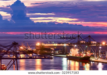Background for cranes and industrial cargo ships in port at twilight.