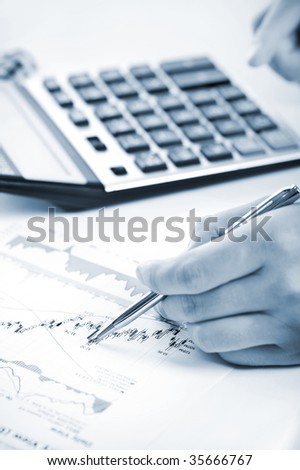 Cold tone sepia image of a man\'s hand with pen analyzing stock charts