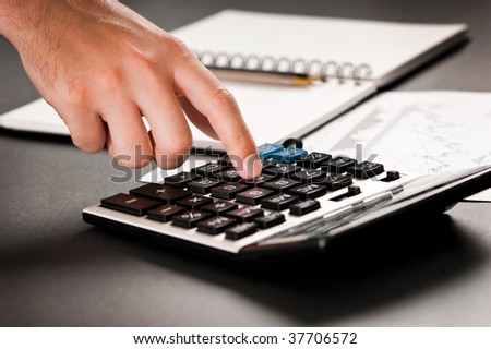 Close-up of hand pressing button on calculator in an office environment