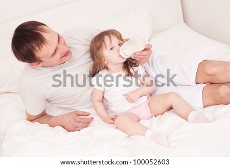 happy family;  father feeding his daughter with milk  in bed at home