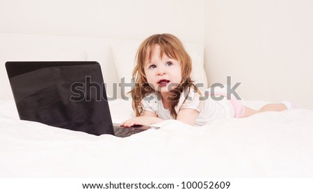 happy one year old girl with a laptop in bed at home