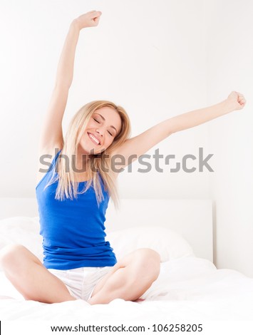 beautiful happy young woman waking up in the morning and stretching  in bed at home