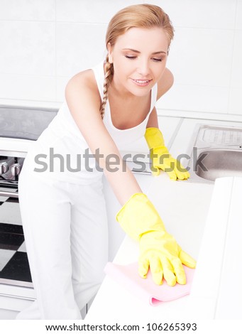 beautiful  young housewife wearing gloves cleaning the furniture  in the kitchen at home