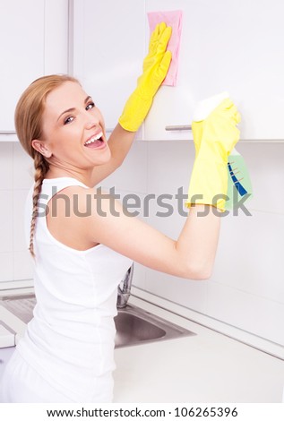 beautiful  young housewife wearing gloves and holding detergent, cleaning the furniture  in the kitchen at home