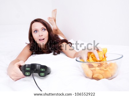 pretty woman playing computer games and eating potato chips in bed at home