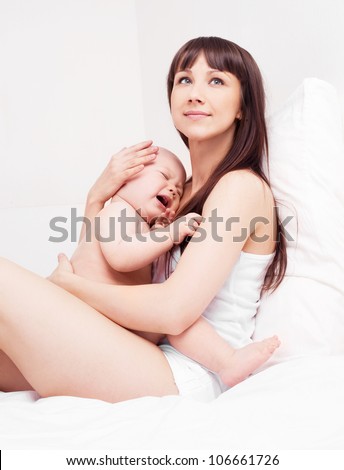 happy young mother and her crying one year old daughter in bed at home