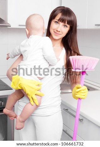 beautiful  young woman holding her baby and cleaning the furniture in the kitchen