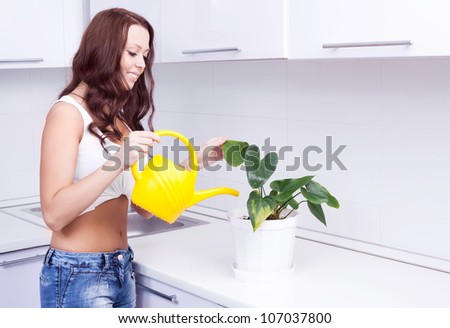 beautiful happy young housewife watering the flowers in pots  in the kitchen at home