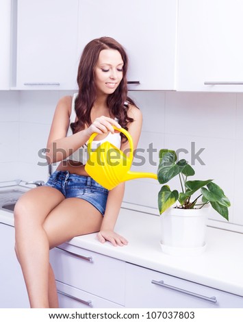 beautiful happy young housewife watering the flowers in pots  in the kitchen at home