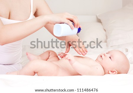 Mother applying baby powder before putting diapers on her four month old baby in bed at home